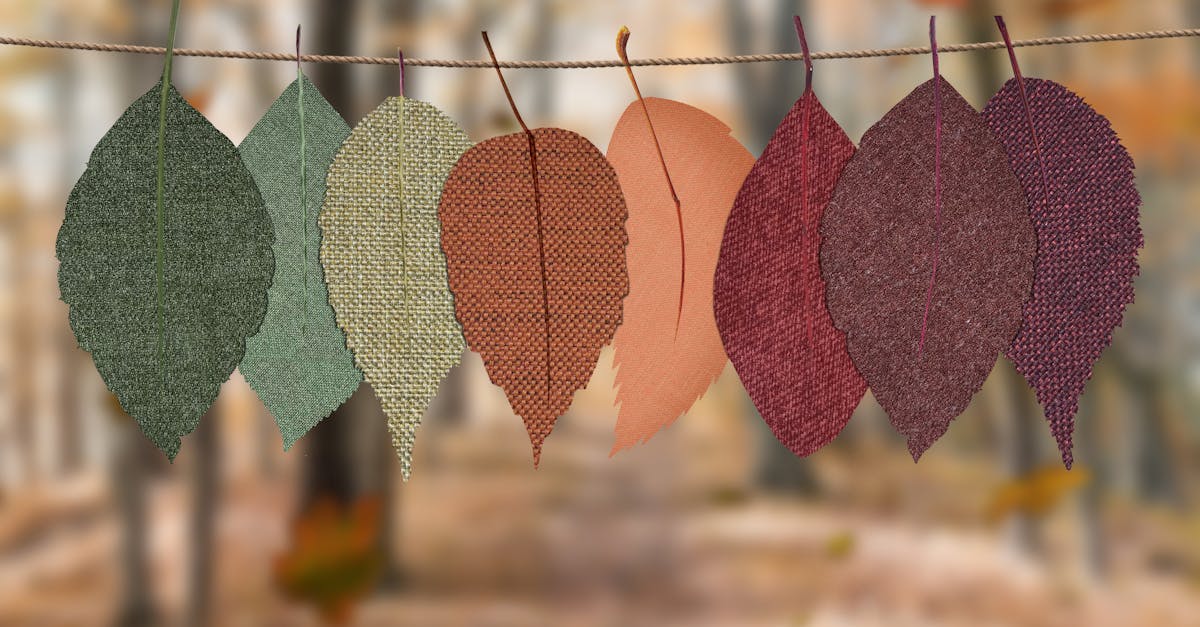 Fabric leaves hang on a rope, showcasing autumn colors in a forest backdrop.