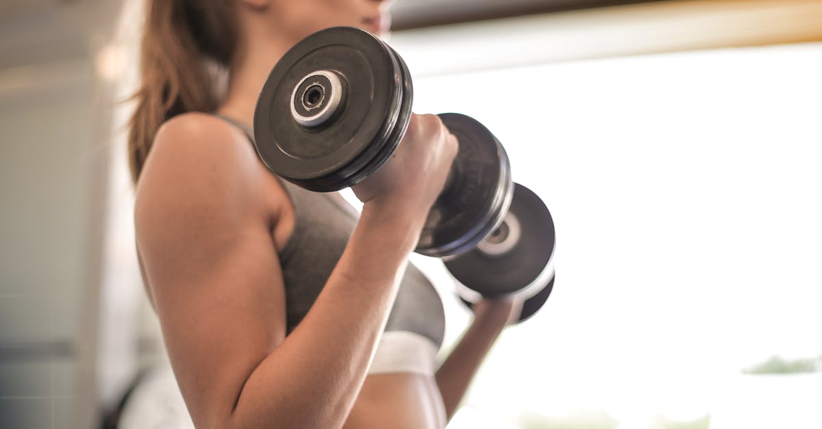Focused woman lifting dumbbells in a bright gym, emphasizing strength and fitness.